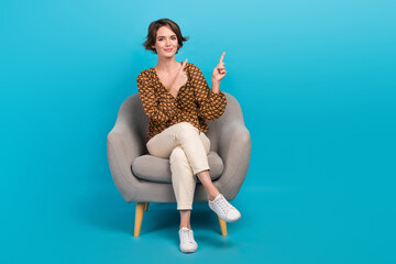 Full body portrait of charming positive lady sit comfort chair indicate fingers empty space...