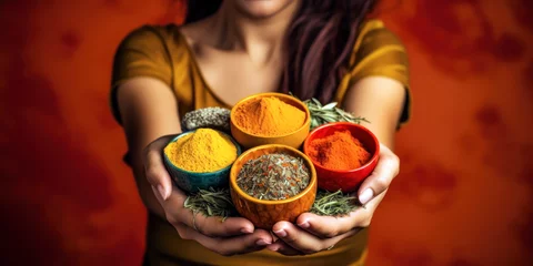 Rolgordijnen A woman holding vibrant colored spices in her hands on a solid orange background. © MADMAT