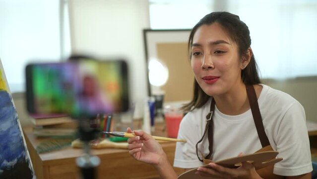 
Artist teaching live stream online class painting with paint brush on canvas work art and oil painting by smartphone. Art teacher woman teaching creative painting class online for students learning.