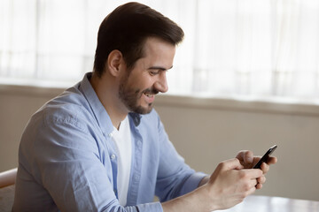 Happy laughing man looking at phone screen, browsing mobile device apps, reading good news in email or social network message, playing game, enjoying leisure time with smartphone