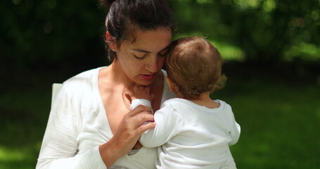 Mother cuddling and loving baby infant outside at park nature