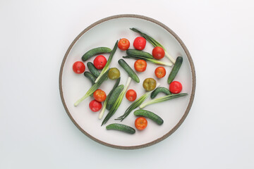 Tomatoes, cucumbers and green onions on a round white plate with a dark rim. Mini vegetables in a plate.