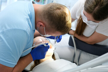 latest technology cleaning and whitening teeth nurse and doctor treating the teeth of a young female patient teenager masks gloves cleanliness sanitation. latest device in dental office in a clinic