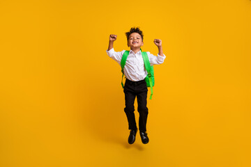 Fototapeta na wymiar Full length photo of small beautiful schoolboy wear stylish shirt rucksack jump clenching fists isolated on yellow color background