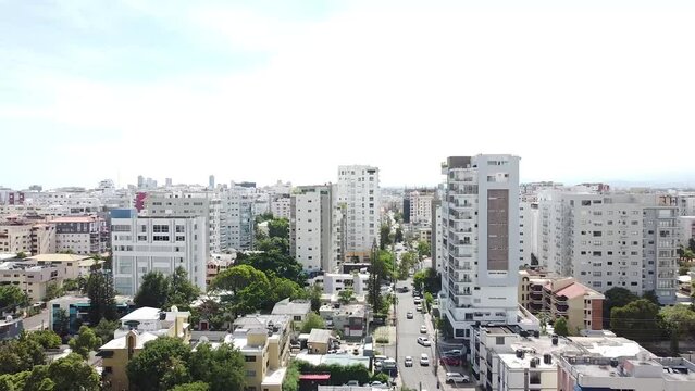 Drone vuelan por encima de la calle entre edificios modernos de altura con fachadas. dia soleado con trafico.