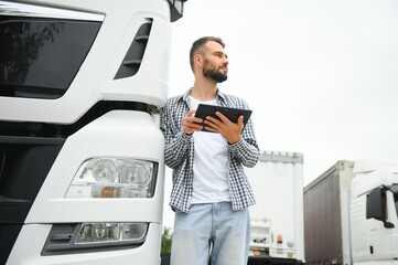 Young handsome truck driver is standing with a tablet near the truck