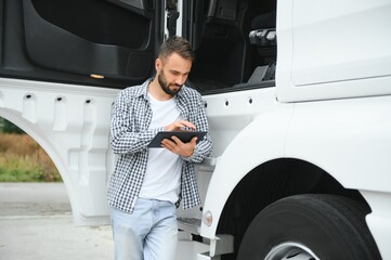 Young handsome truck driver is standing with a tablet near the truck