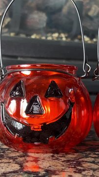 Two bright orange candlesticks in the form of pumpkins Jack-o-lantern Glass lantern with real candles. Black eyes and black smile Transparent orange glass Standing in front of a fireplace