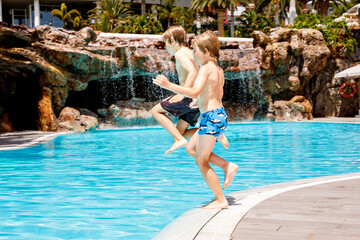 Two happy little kids boys jumping in the pool and having fun on family vacations in a hotel...