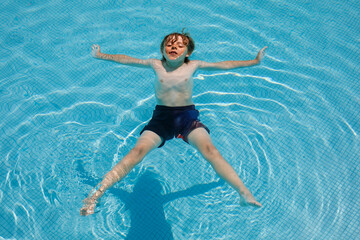 Portrait of happy little kid boy in the pool and having fun on family vacations in a hotel resort. Healthy child playing in water, swimming and splashing.