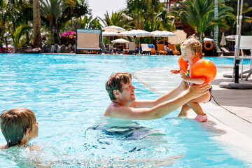 Cute happy little toddler girl, school kid boy and father in the pool and having fun on family...