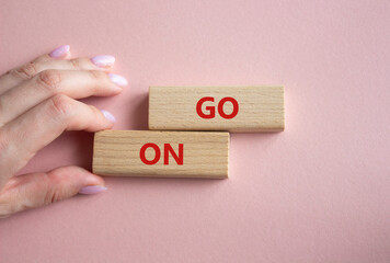 Go on symbol. Wooden blocks with words Go on. Businessman hand. Beautiful pink background. Business...