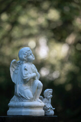 Fototapeta na wymiar Zwei kleine Engelsfiguren vor grünem Naturhintergrund auf Friedhof, keine Namen