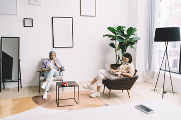 Focused daughter browsing netbook while mother reading novel in living room