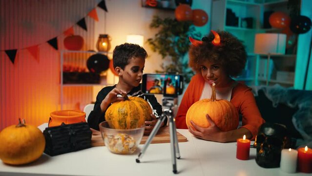 Beautiful mom and cute little son record a video about Halloween pumpkin carving. African American family dressed in costumes spend time together at home and get ready for a Halloween holiday