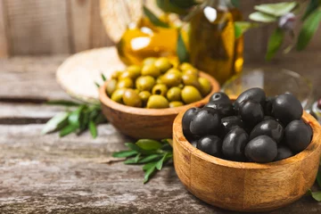 Tuinposter Set of black and green olives on a white wooden background. Various types of olives in wooden bowls and fresh olive leaves. Copy space. Place for text. flat lei. Delicatessen. © Avocado_studio