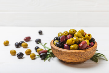 Set of green, red and black olives on a white wooden background. Various types of olives in wooden bowls and fresh olive leaves. Copy space. Place for text. flat lei. Delicatessen.