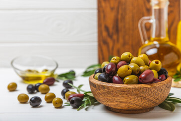 Set of green, red and black olives on a white wooden background. Various types of olives in wooden bowls and fresh olive leaves. Copy space. Place for text. flat lei. Delicatessen.