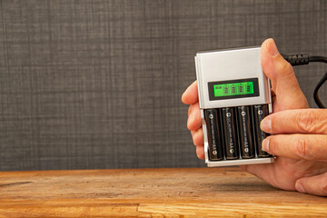 Four rechargeable batteries in a battery charger. Hands placing a battery in a charger with a green display showing the level of charge. NI-MH and LI-MH lithium battery. Copy space. - obrazy, fototapety, plakaty