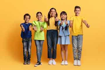 Cute school aged kids posing on yellow, showing thumb ups