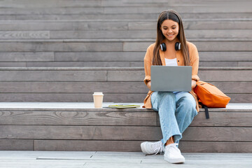 Cheerful young woman student working on project, using laptop outdoors