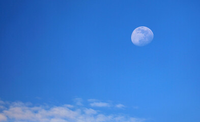 White moon almost full and blue sky with some clouds at daytime