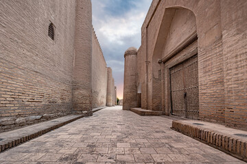 Street between high walls of ancient madrasa with towers and carved wooden gate, Khiva, Uzbekistan