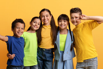 Cute happy multiracial kids taking selfie on yellow background
