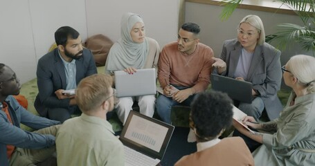 Diverse group of colleagues discussing business project sitting in circle and talking in coworking center. Professional discussion and people concept.