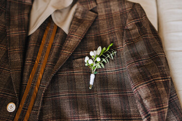 A stylish brown men's checkered jacket with a boutonniere of flowers lies on the sofa in the...