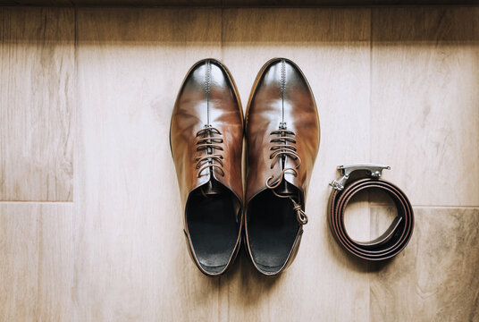 Men's brown leather shoes and a black belt lie on the floor. Photo, top view.