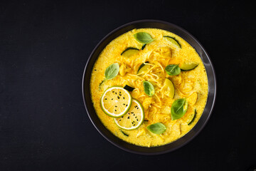 Curry soup with chicken meat, zucchini and chow mein  noodles on black background
