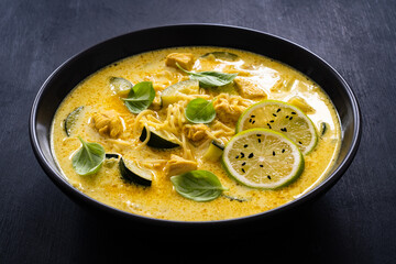 Curry soup with chicken meat, zucchini and chow mein  noodles on black background