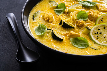 Curry soup with chicken meat, zucchini and chow mein  noodles on black background