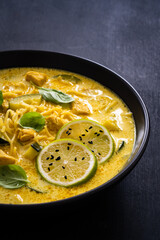 Curry soup with chicken meat, zucchini and chow mein  noodles on black background