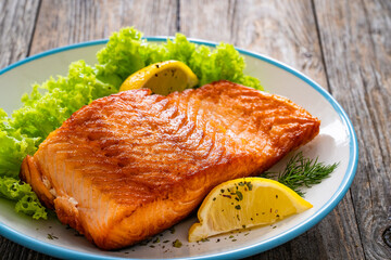 Seared salmon steak with lettuce and lemons on wooden table
