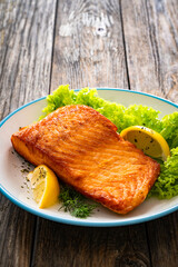 Seared salmon steak with lettuce and lemons on wooden table
