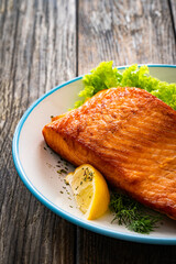 Seared salmon steak with lettuce and lemons on wooden table
