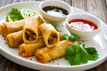 Vegetable filled spring rolls and sauces on wooden table
