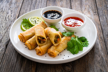 Vegetable filled spring rolls and sauces on wooden table
