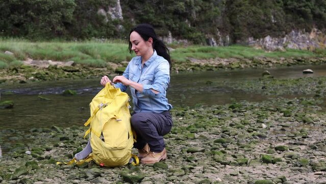 Young woman searching for something in her backpack in the middle of nature