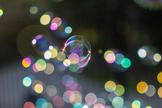 Soap bubbles floating back lit with bokeh creating rainbow of colorful lights