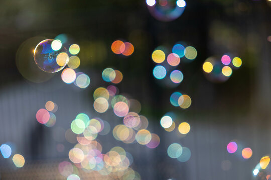 Soap bubbles floating back lit with bokeh creating rainbow of colorful lights