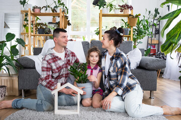 Traditional family with child are enjoying new home, sitting on the sofa and holding the roof. Mortgage, insurance and protection, buying and moving into your own home, green house with potted plant