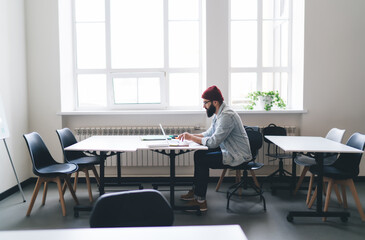 Man in red hat working on laptop at desk in office