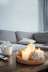 Autumn fall cozy mood composition for hygge home decor. Orange pumpkins, burning candles, cup with hot drink and remote controller on coffee table in living room. Movie night at home. Cozy relax time