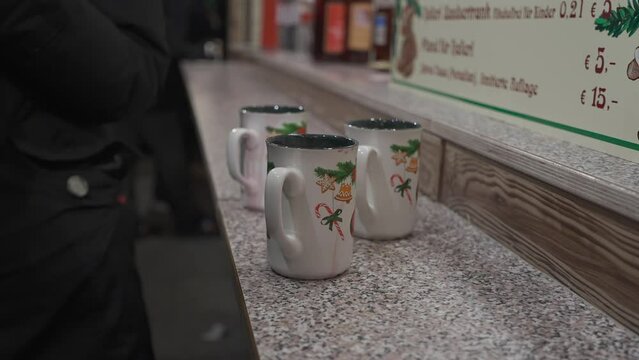 Unrecognizable people drink hot wine from beautiful cups at the Christmas fair in Germany, Munich on Marienplatz in the evening. Hot mulled wine at the Advent market in Muenchen. Weihnachten Gluhwein