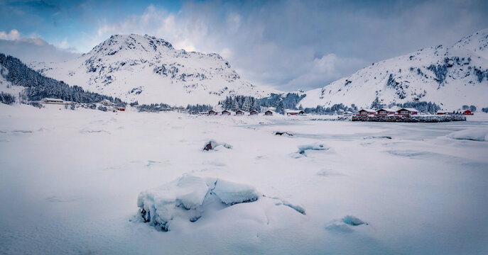 Panoramic winter view of Justad fishing village on Vestvagoy island with snowy peaks on background. Gloomy morning scene of Lofoten Islands after huge snowfall. Traveling concept background.