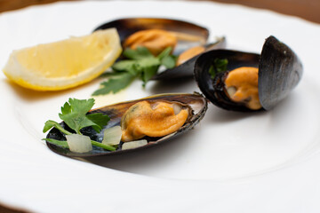 On a plate are large mussels with herbs and a slice of lemon