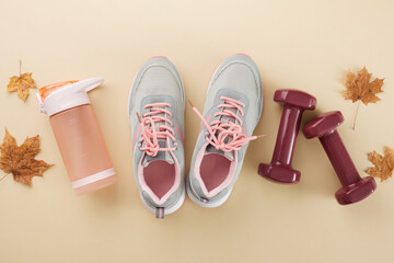 Autumn bodybuilding regimen concept. Top view composition of sneakers, dumbbells, water flask, dry maple leaves on pastel brown background